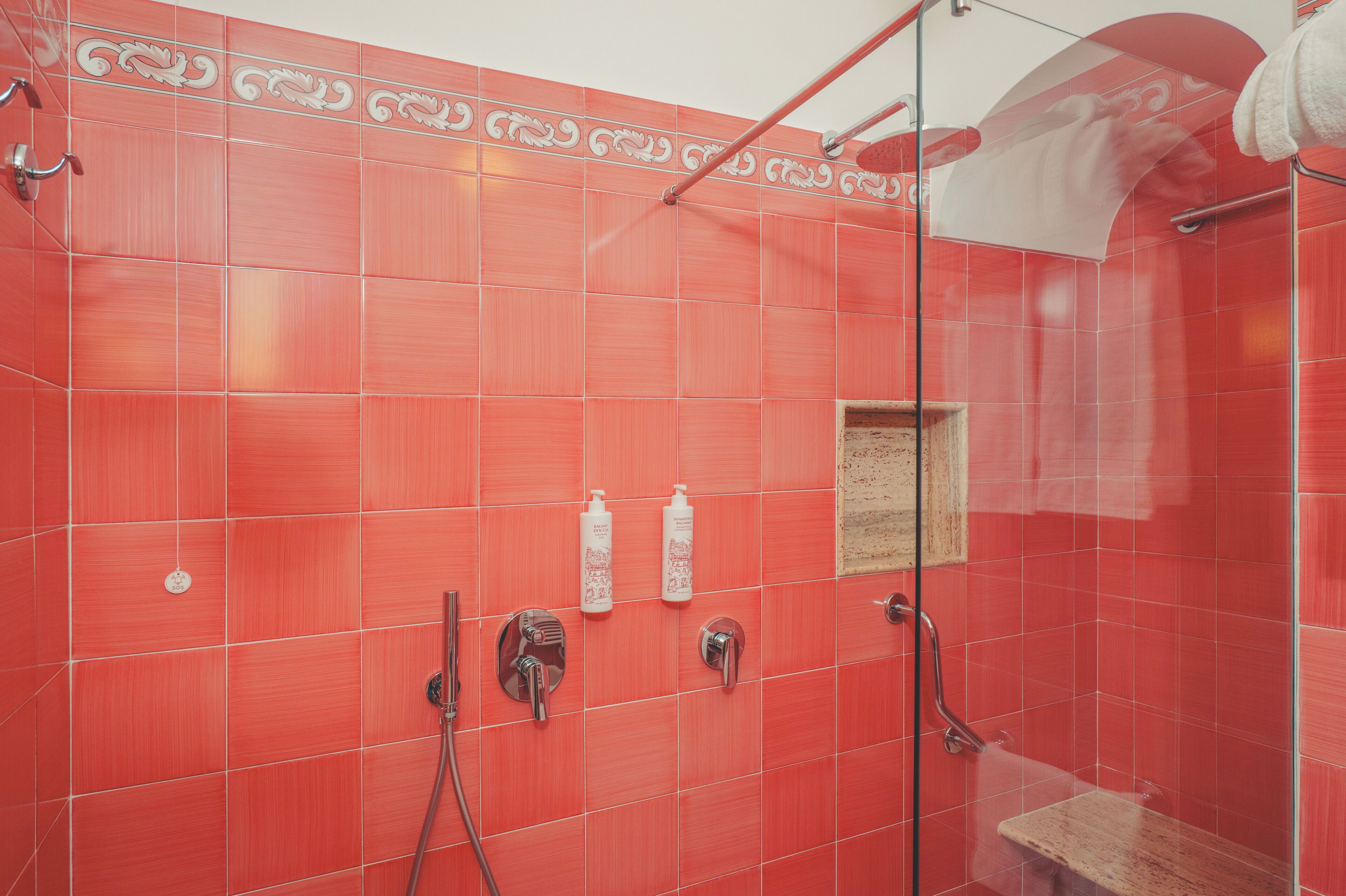 A shower with red tiles, a glass door, and a wooden bench.