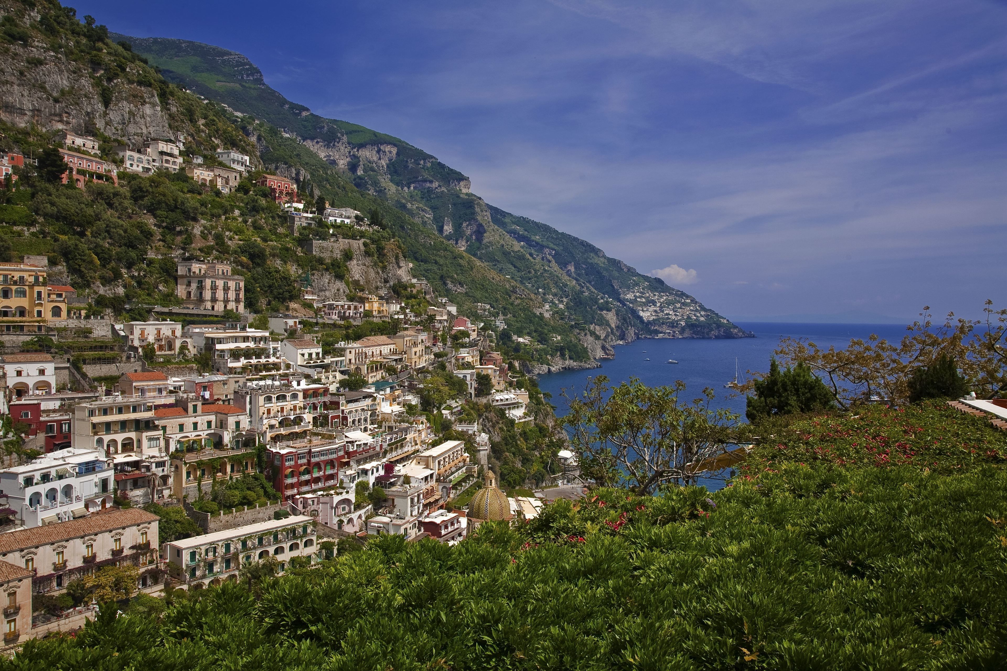 A coastal town with buildings on a hillside, a clear blue sea, and a prominent church with a dome.