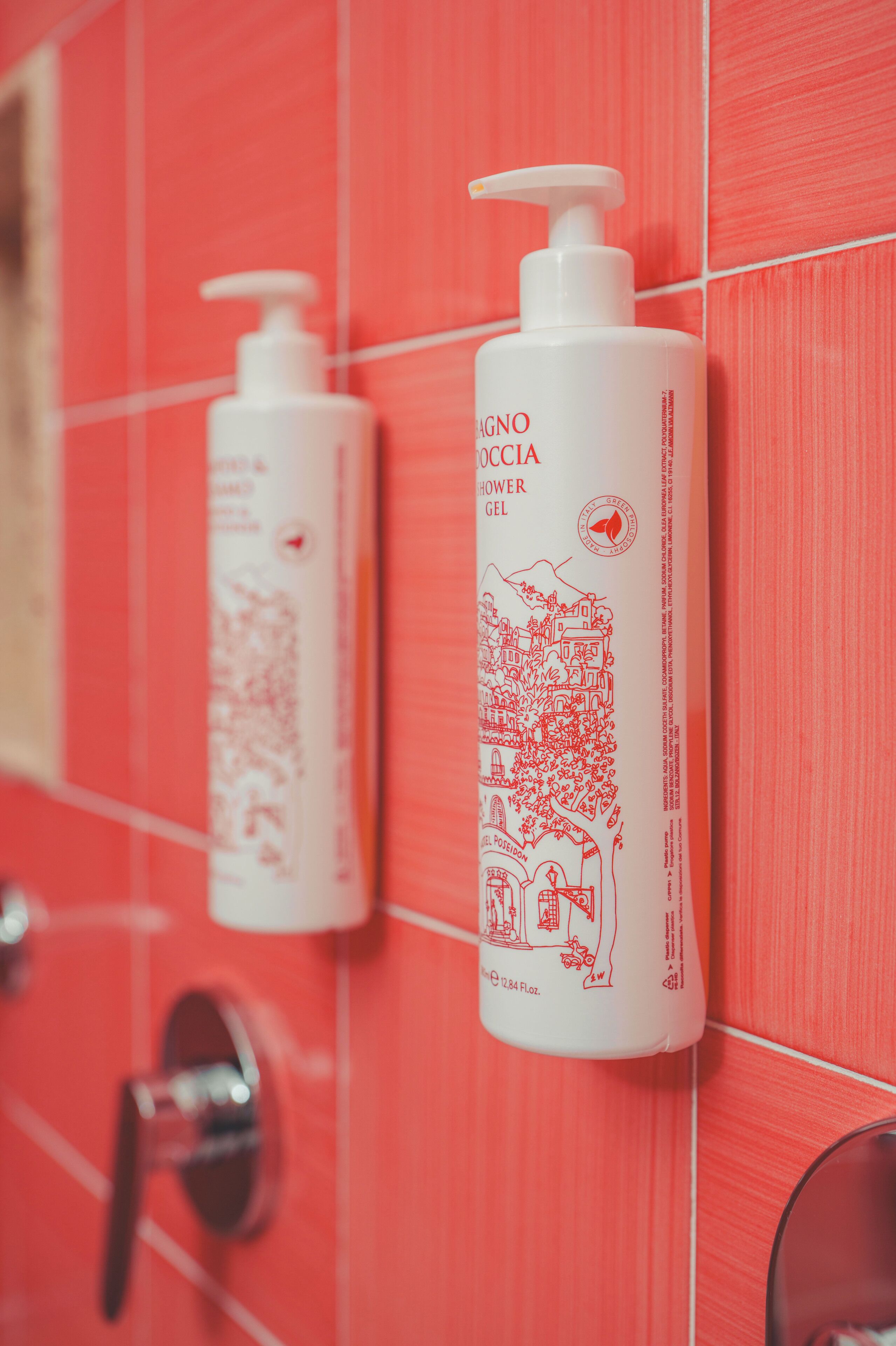 Two white shower gel bottles with red illustrations on a red tiled wall.