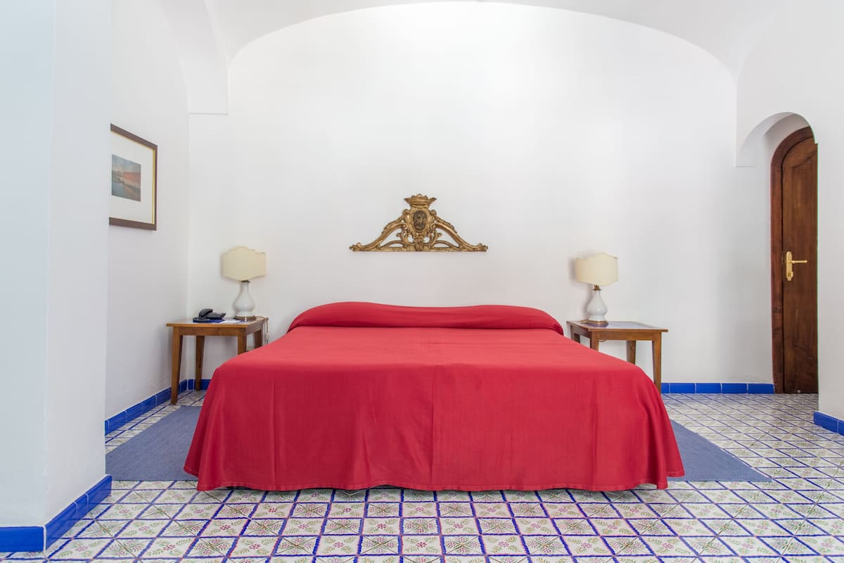 Una habitación con una cama, dos mesitas de noche, una lámpara de pared y una puerta.