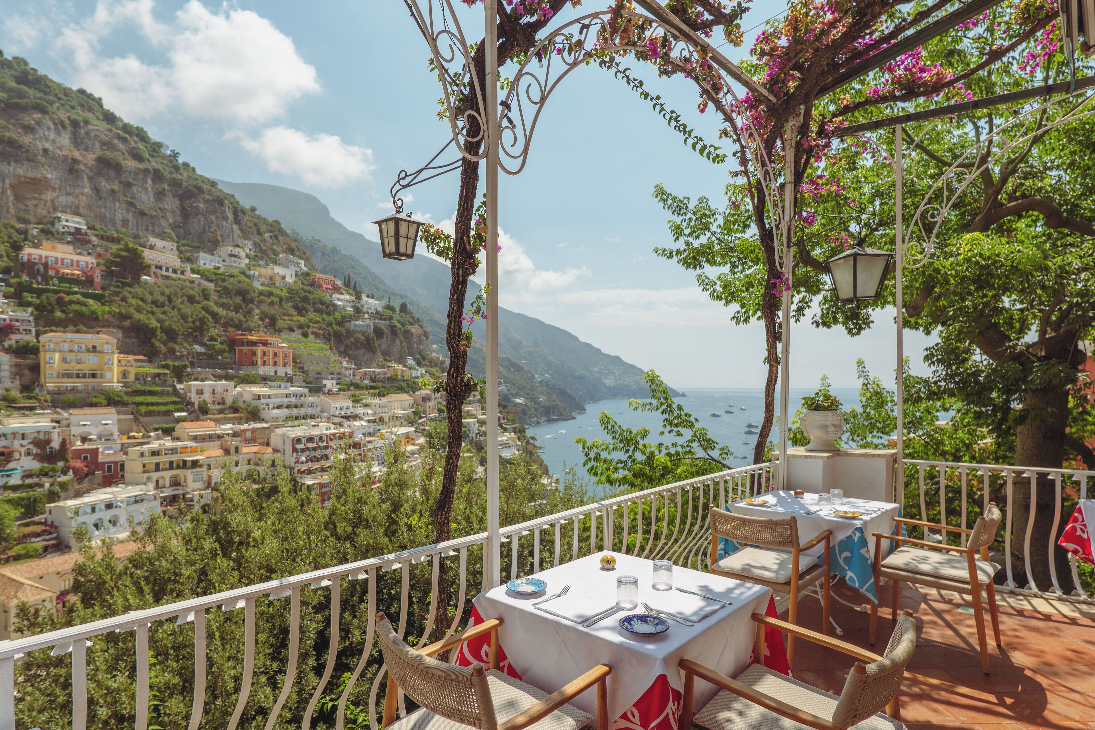 A terrace with a table set for dining, overlooking a coastal town and the sea.