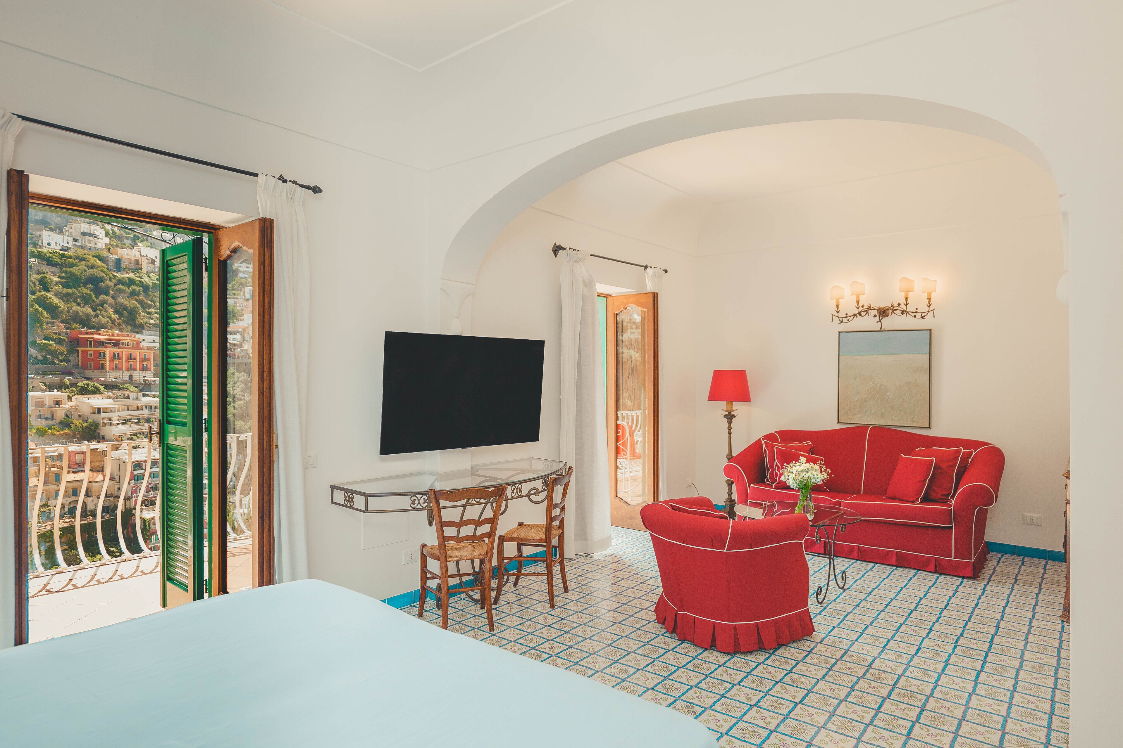 A hotel room with a balcony, a TV, a red sofa, and a patterned floor.