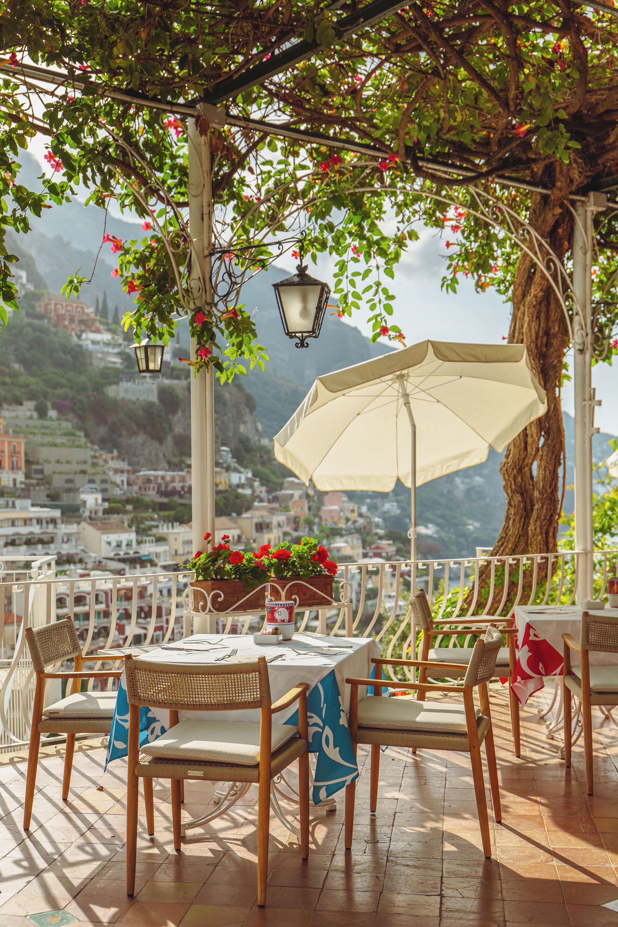 Un patio exterior con sillas de mimbre, una mesa con mantel blanco y faroles colgantes.