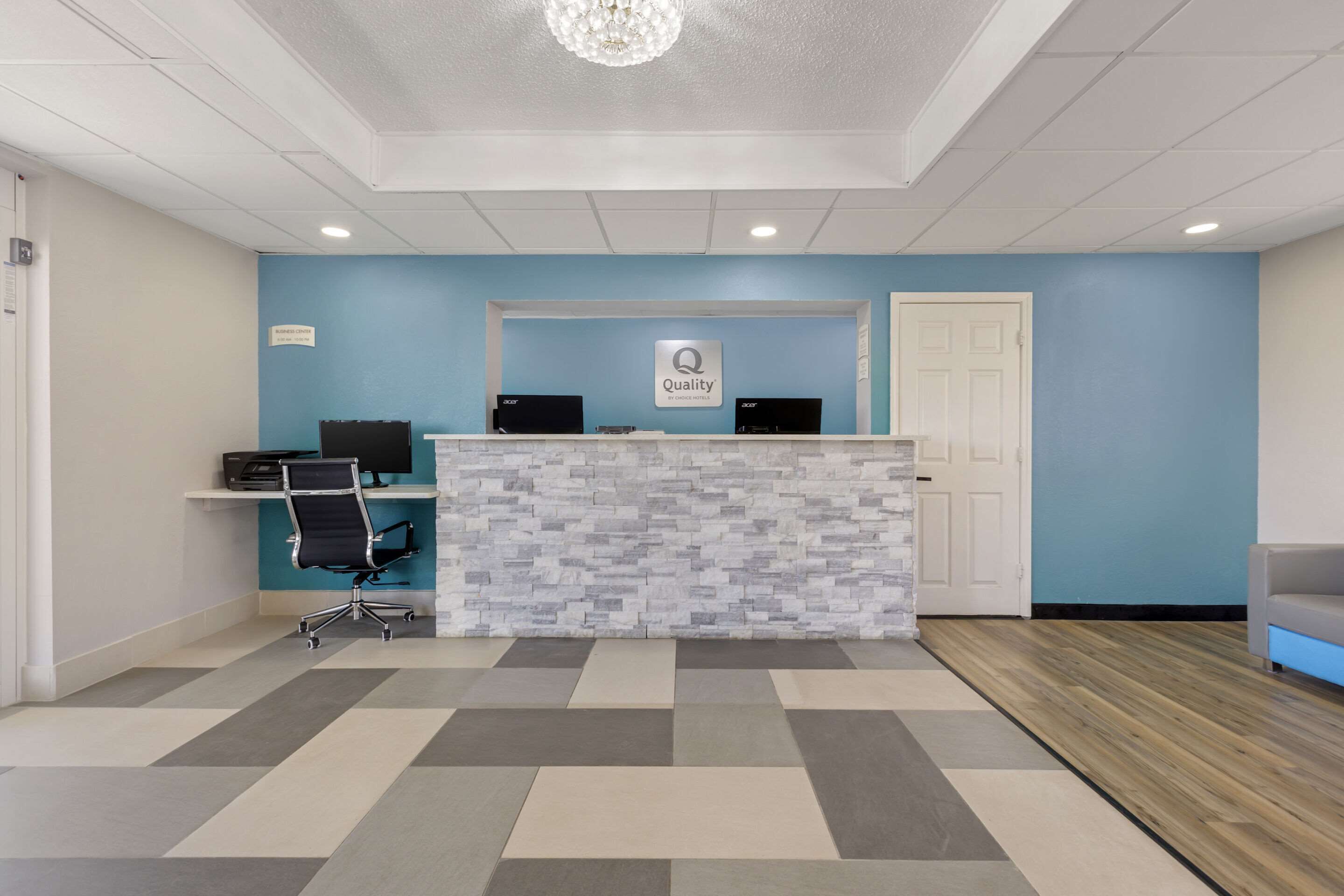 A reception area with a blue wall, a reception desk, two computers, and a black office chair.