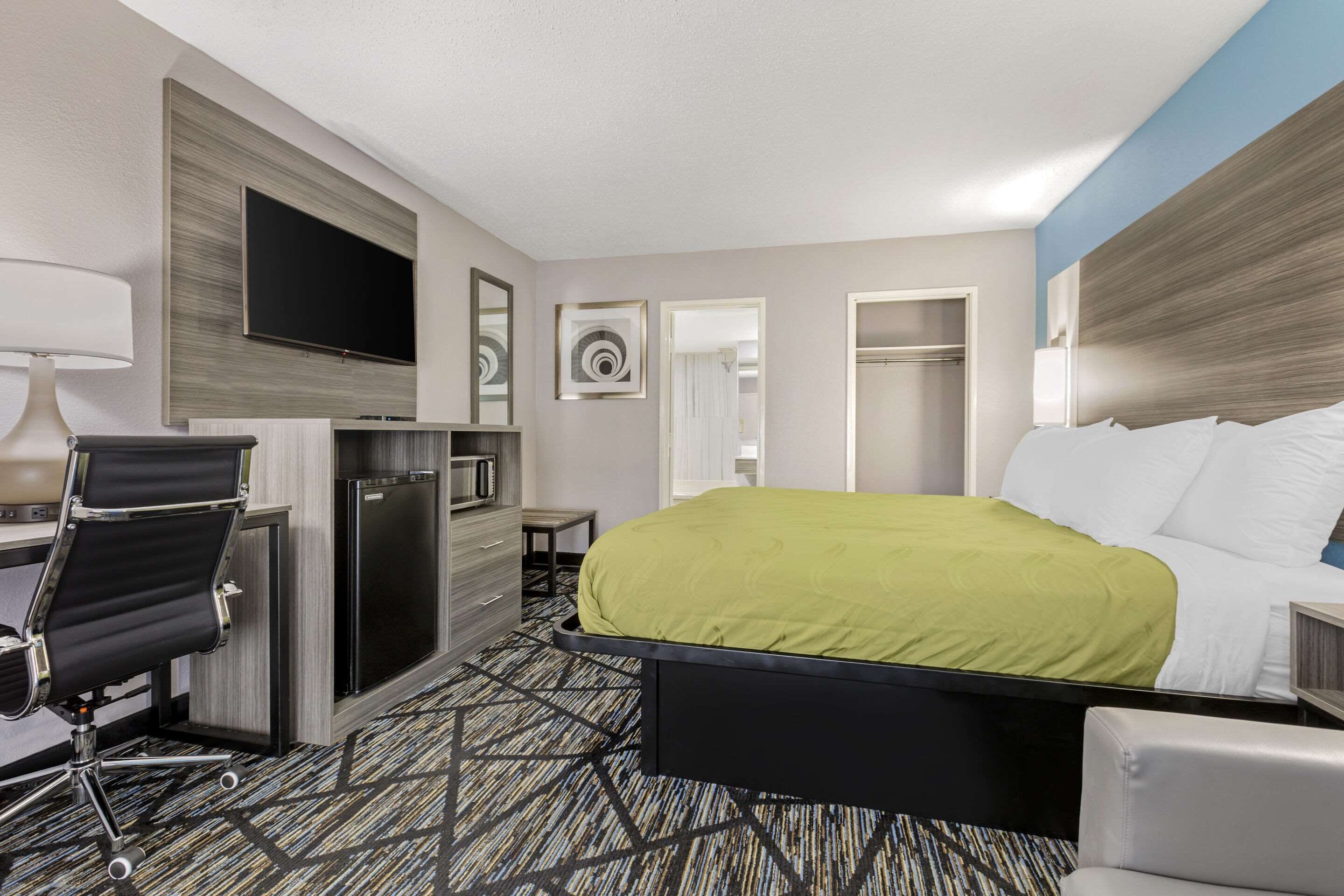 A hotel room with a bed, a desk with a chair, a TV, a mirror, and a wardrobe.