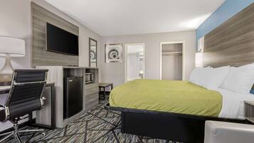 A hotel room with a bed, a desk with a chair, a TV, a mirror, and a wardrobe.