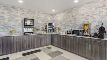 A modern kitchen with grey cabinets, a microwave, a coffee machine, and a TV on a stone-textured wall.