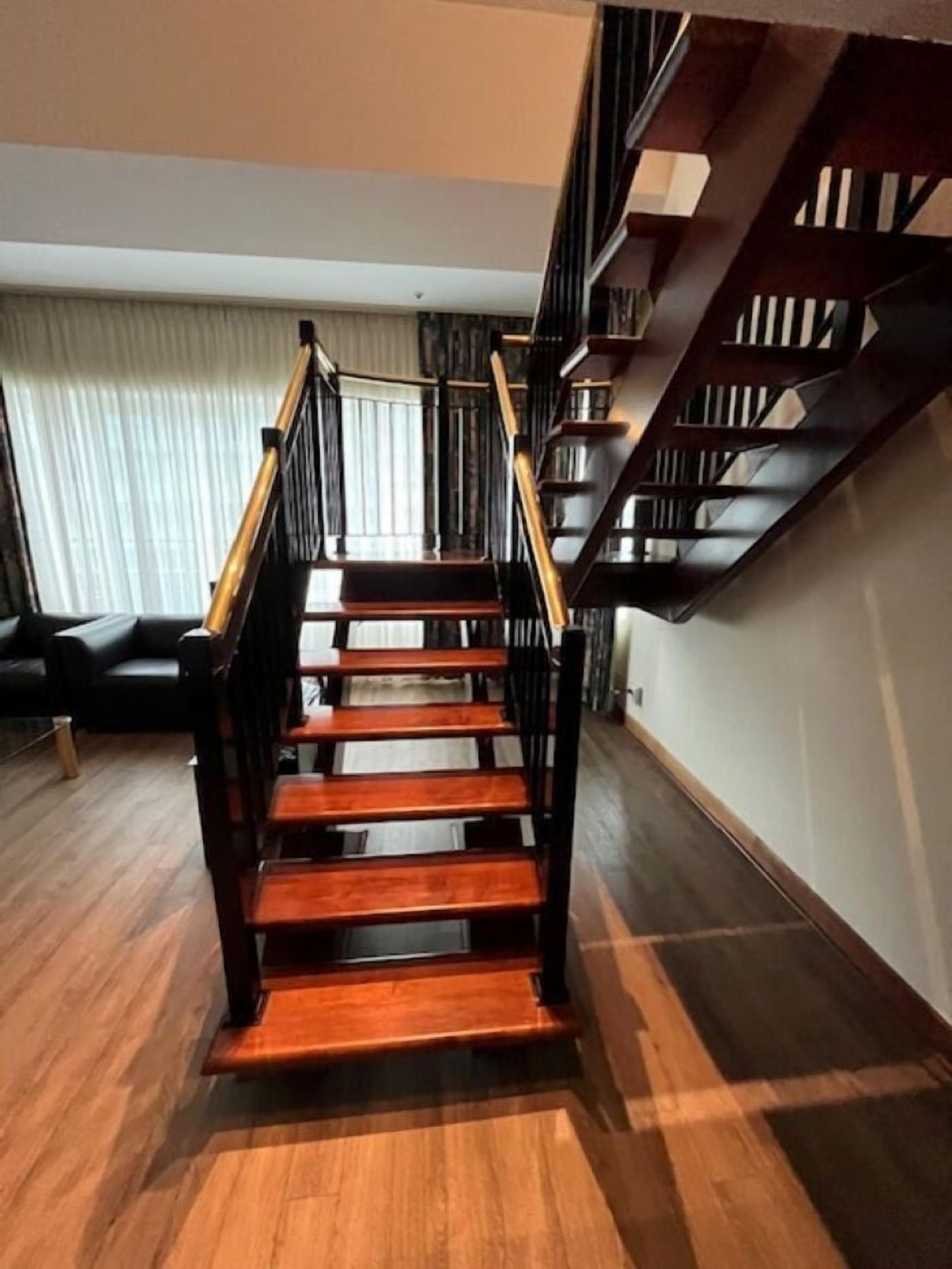 A wooden staircase with black railings and a handrail, leading to an upper floor.