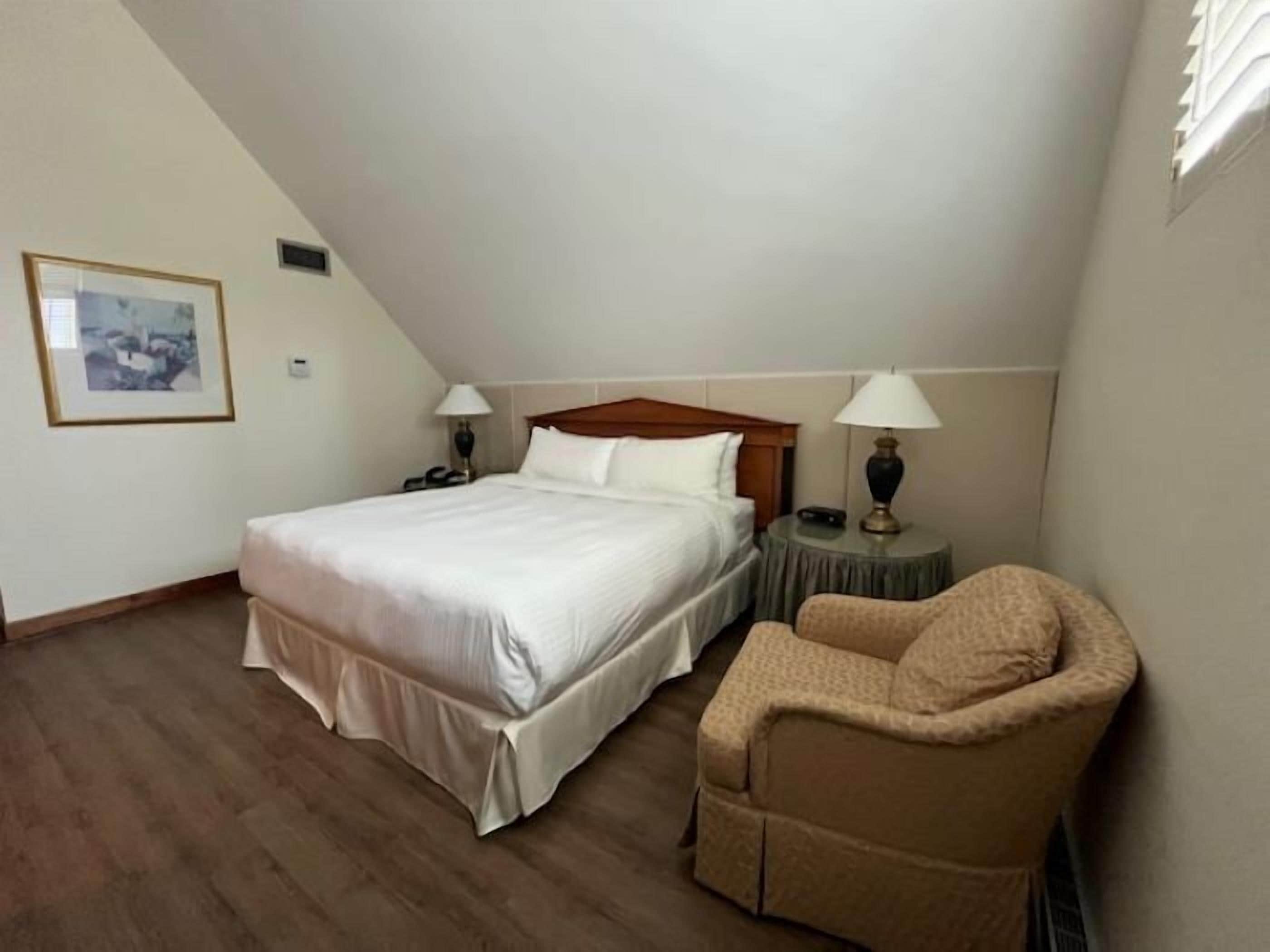 Un dormitorio con una cama grande, dos mesitas de noche con lámparas, una silla e imagen enmarcada en la pared.