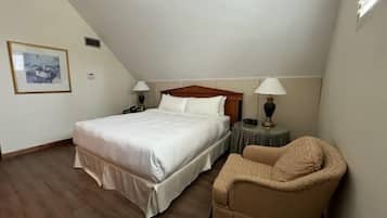 A bedroom with a large bed, two bedside tables with lamps, a chair, and a framed picture on the wall.
