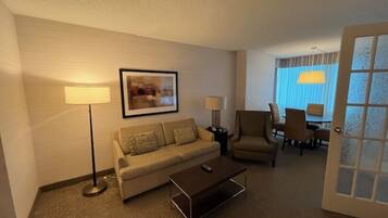 A hotel room with a sofa, a coffee table, a side table, a lamp, a chair, and a dining table with chairs.