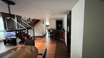 Un intérieur moderne avec une table à manger en bois, des chaises, un escalier et un coin cuisine.