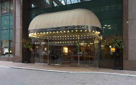 The Cambridge Suites Hotel entrance with a glass facade, a curved awning, and a reflection of cars in the glass.