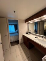 Een hotelbadkamer met een grote spiegel, een wastafel en een deur naar een slaapkamer.