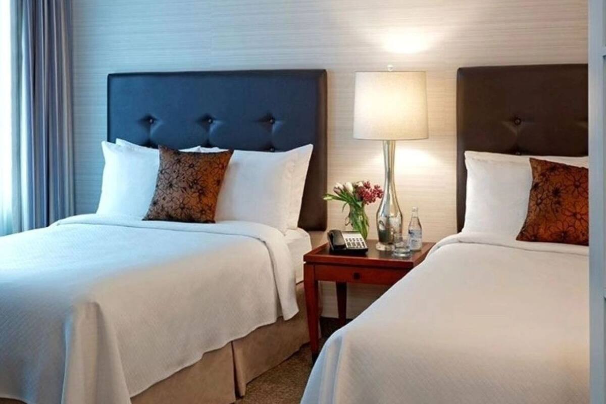 A hotel room with two beds, a nightstand with a lamp, and a vase with flowers.