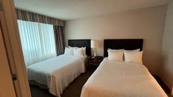 A hotel room with two beds, a nightstand with a lamp, and a window with curtains.