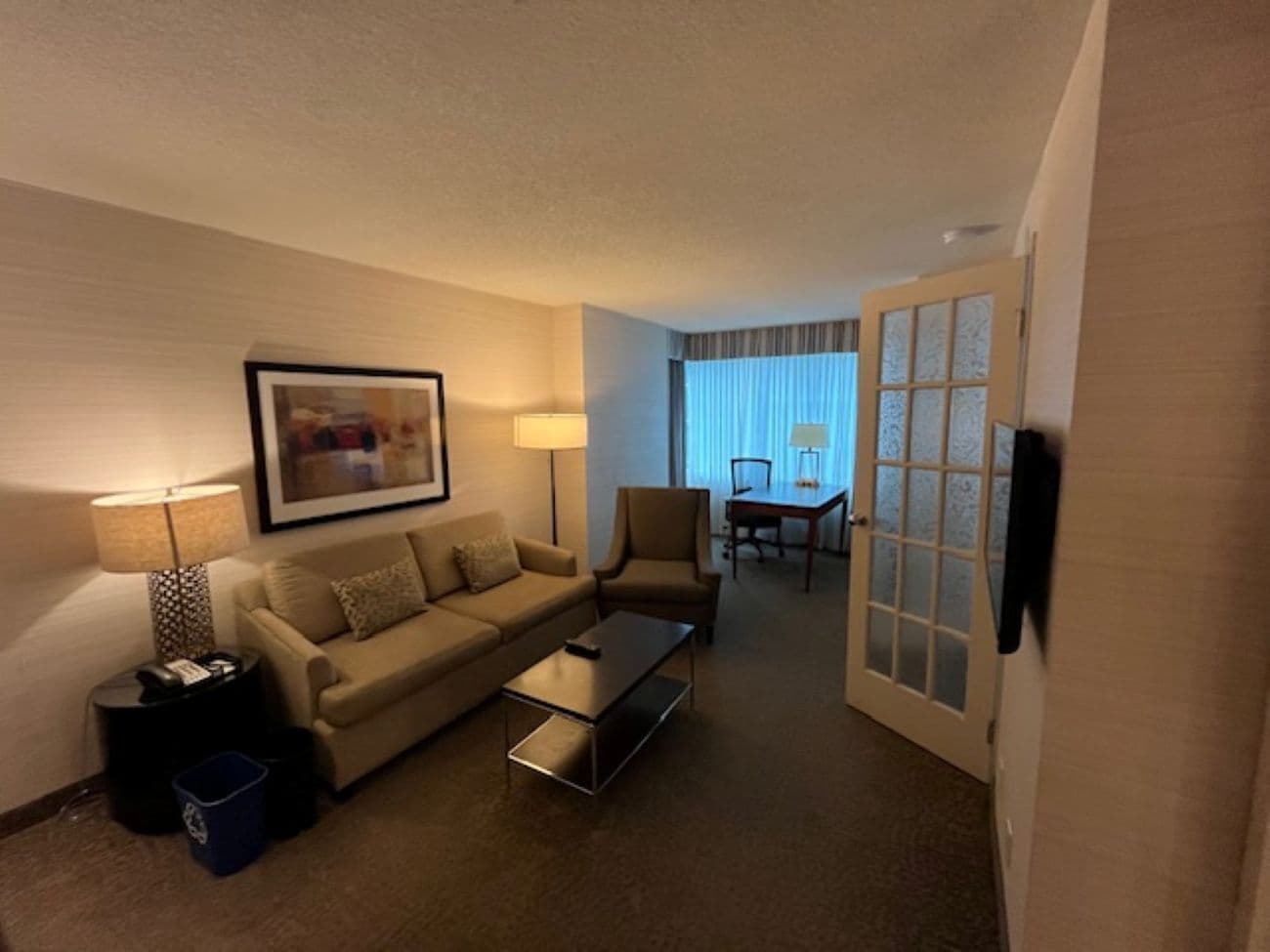 A hotel room with a sofa, armchair, coffee table, and a dining table with chairs.