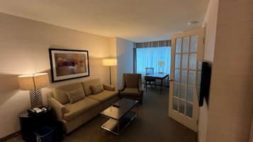 Ein Hotelzimmer mit Sofa, Ohrensessel, Couchtisch und Esstisch mit Stühlen.