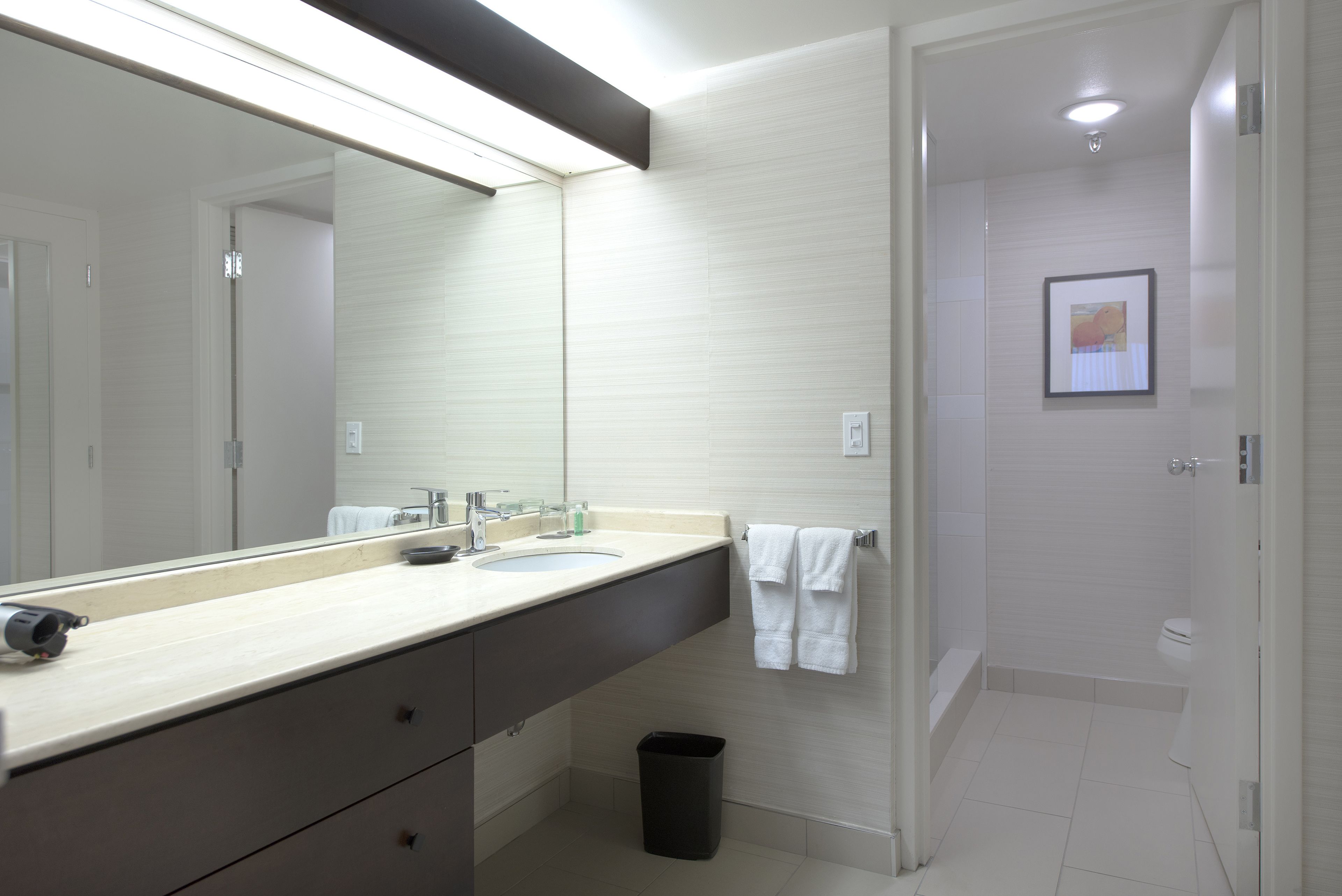 Un baño moderno con un espejo grande, dos lavamanos, un perchero para toallas y una zona de ducha.