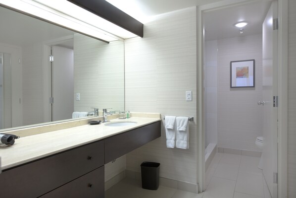 A modern bathroom with a large mirror, two sinks, a towel rack, and a shower area.