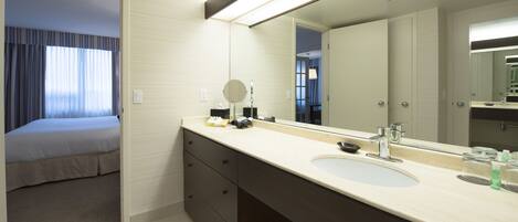 Un baño de hotel con un espejo grande, un lavabo y una cama en la habitación contigua.