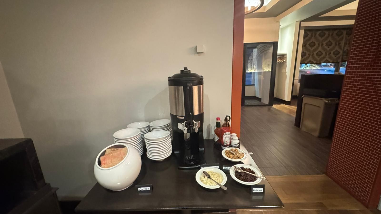 A breakfast buffet setup with a coffee maker, plates, bowls, and condiments.