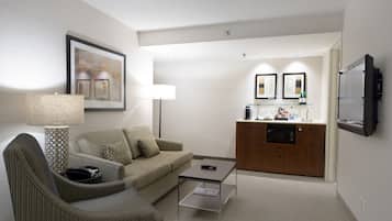 Une chambre d’hôtel de taille réduite, comprenant un canapé, un fauteuil, une table basse et un coin cuisine.