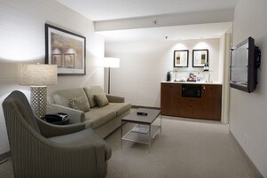Habitación de hotel compacta con sofá, sillón, una mesa de centro y una pequeña cocina.