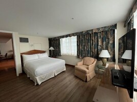 Een hotelkamer met een groot bed, een stoel, een bureau met lamp en een raam met gordijnen.