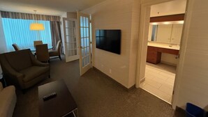 Una habitación de hotel con sala de estar, televisión, sofá y comedor con mesa y sillas.