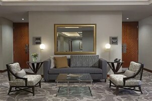 Un hall con un sofá gris, dos sillones, una mesa de centro y un espejo grande en la pared.