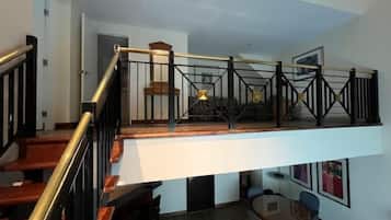 A modern loft-style apartment with a wooden staircase, a mezzanine level, and a dining area.