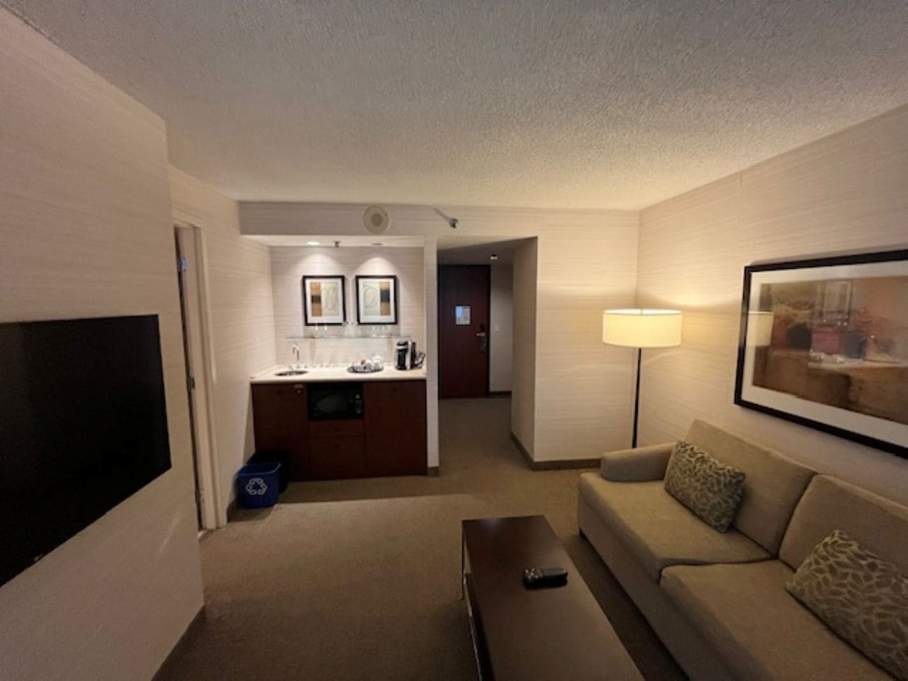 A hotel room with a living area, kitchenette, and a TV mounted on the wall.