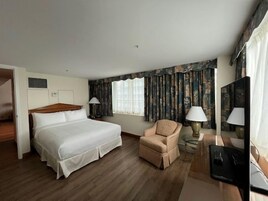 Hotelkamer met een groot bed, een stoel, een bureau met een computer en een raam met gordijnen.