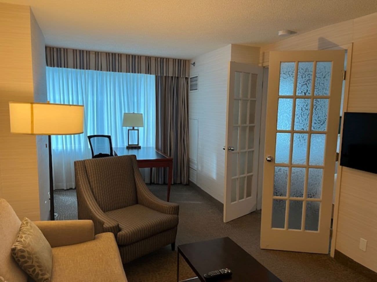 Habitación de hotel con sofá, sillón, mesa de comedor y televisor.