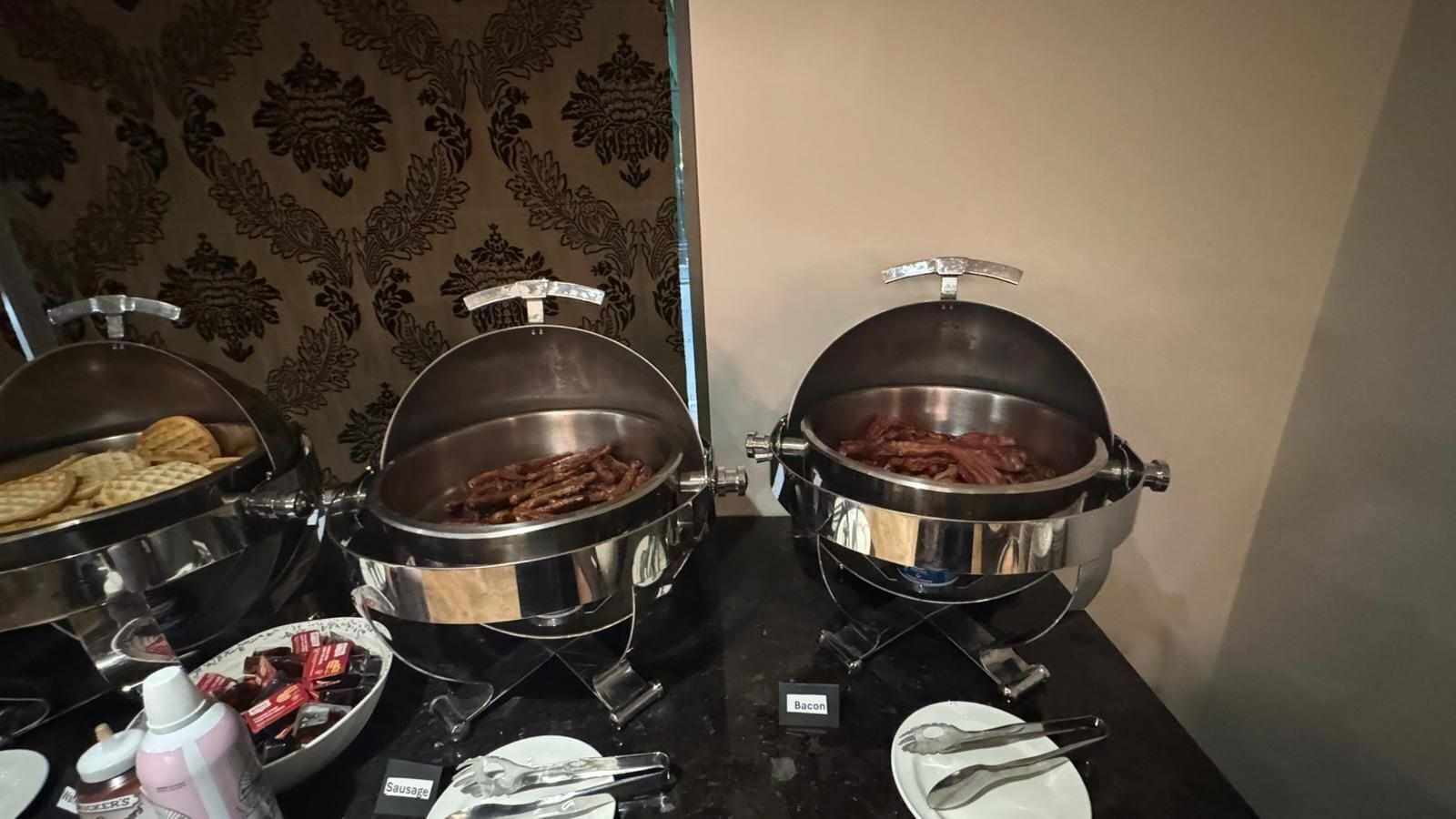 A buffet table with covered dishes of bacon and sausage.