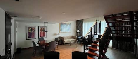 A spacious living room with a staircase leading to a library.