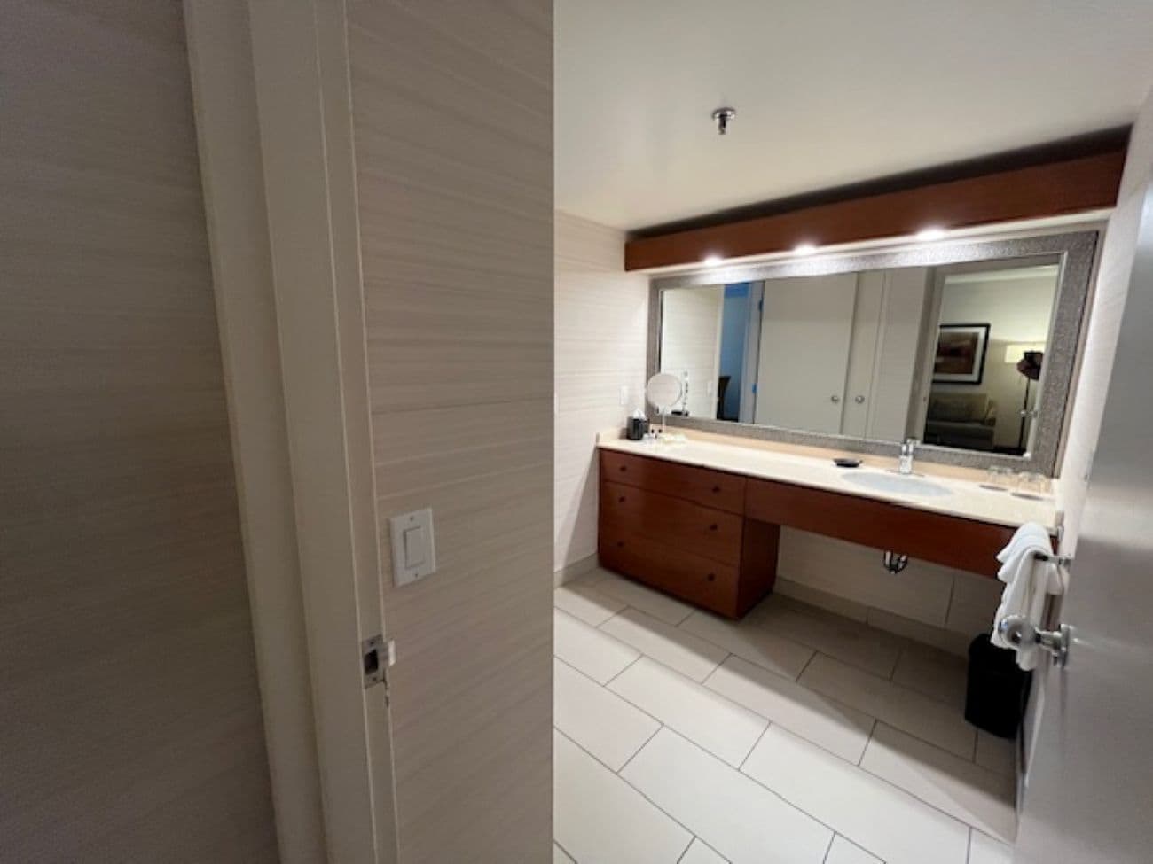 A modern bathroom with a large mirror, wooden vanity, and a tiled floor.