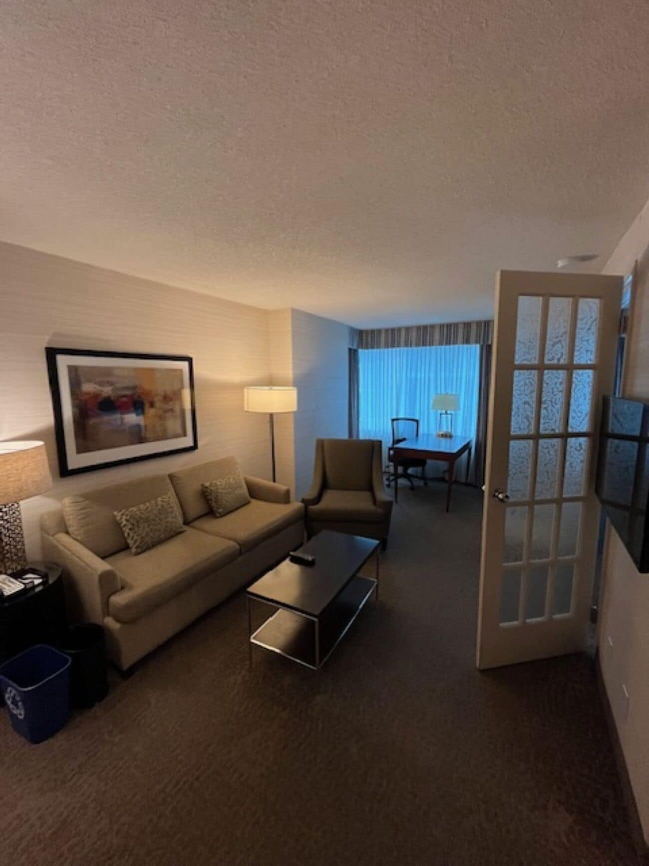 Habitación de hotel con sofá, sillón, mesa de centro y un área de comedor con mesa y sillas.