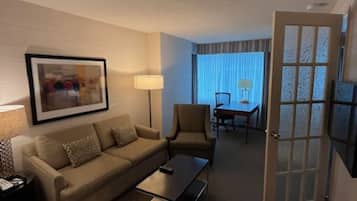 Habitación de hotel con sofá, sillón, mesa de centro y un área de comedor con mesa y sillas.