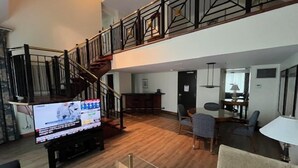 A spacious living area with a wooden floor, a staircase with a black railing, a flat-screen TV on a stand, and a dining area with chairs and a table. - Cambridge Suites Toronto (Toronto)