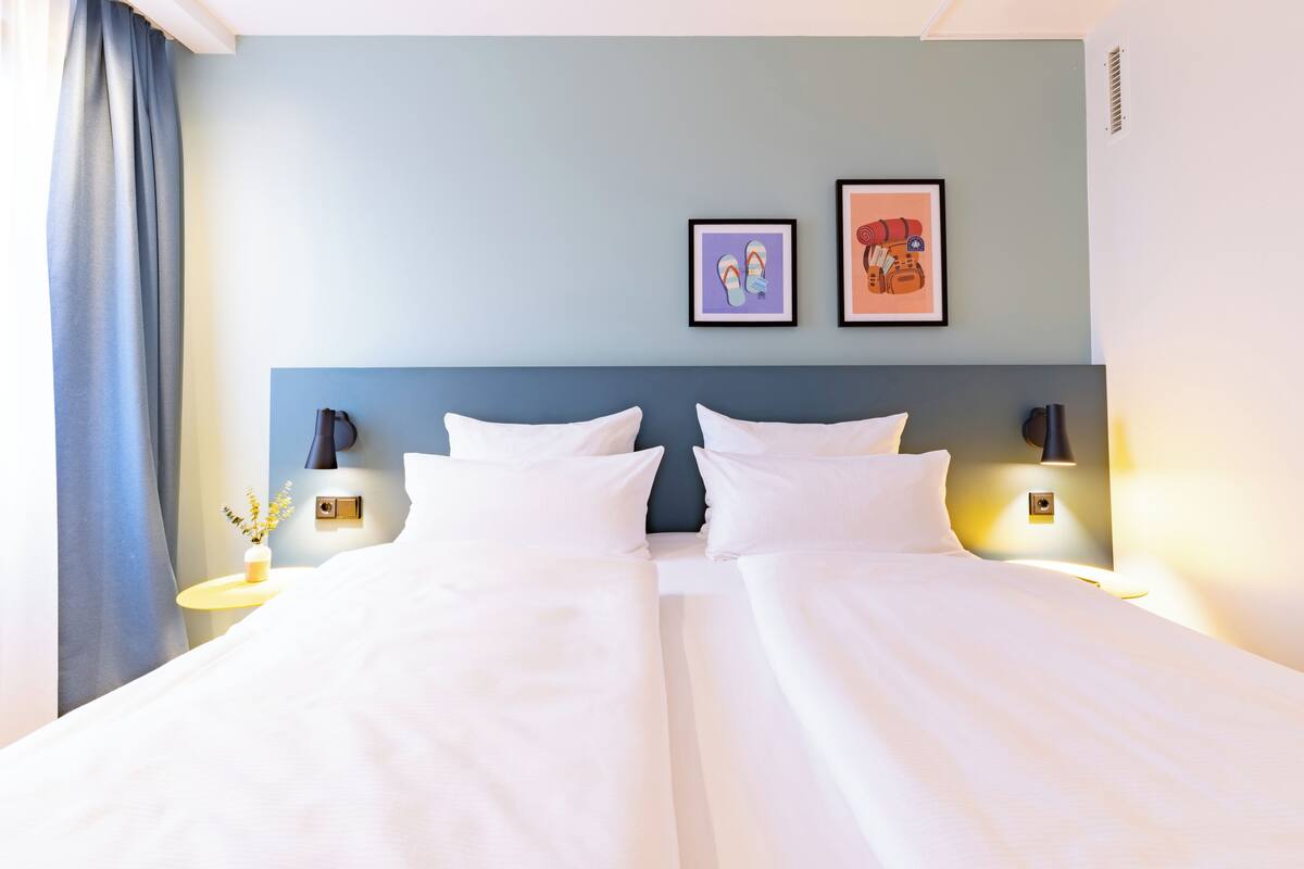 Una habitación de hotel con una cama grande, dos mesitas de noche con lámparas, una obra de arte colgada en la pared y una ventana con cortinas.