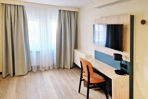 A room with a wooden desk, a chair, a television mounted on the wall, and a radiator.