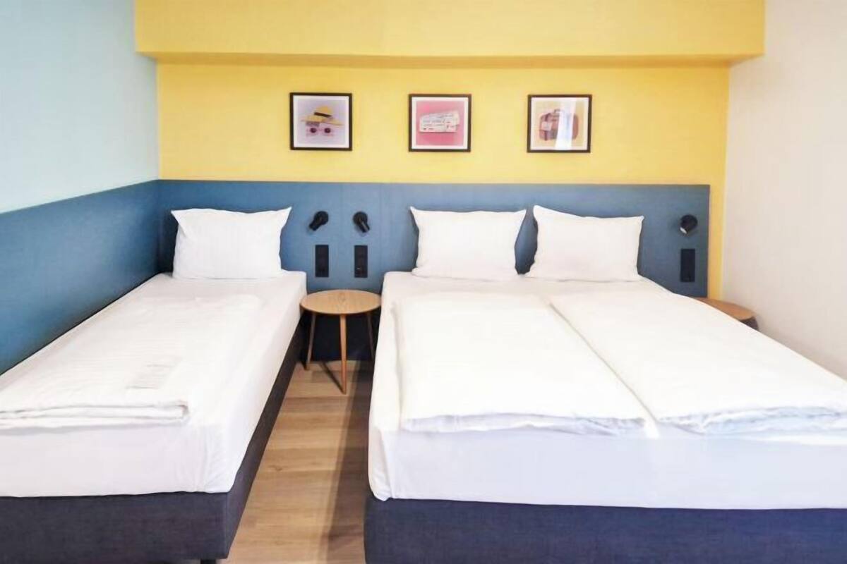 Una habitación con dos camas individuales, una mesita redonda pequeña y una pared con tres cuadros enmarcados.