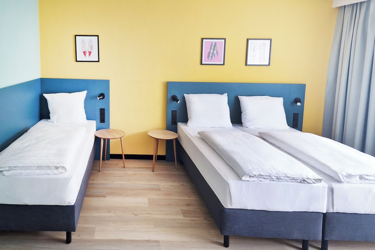 Une chambre d’hôtel avec deux lits simples, une petite table ronde et deux tableaux encadrés accrochés au mur.
