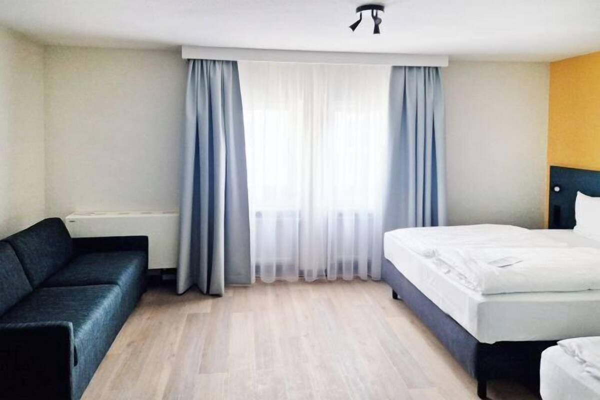 Habitación de hotel con cama, sofá, radiador y ventana con cortinas.