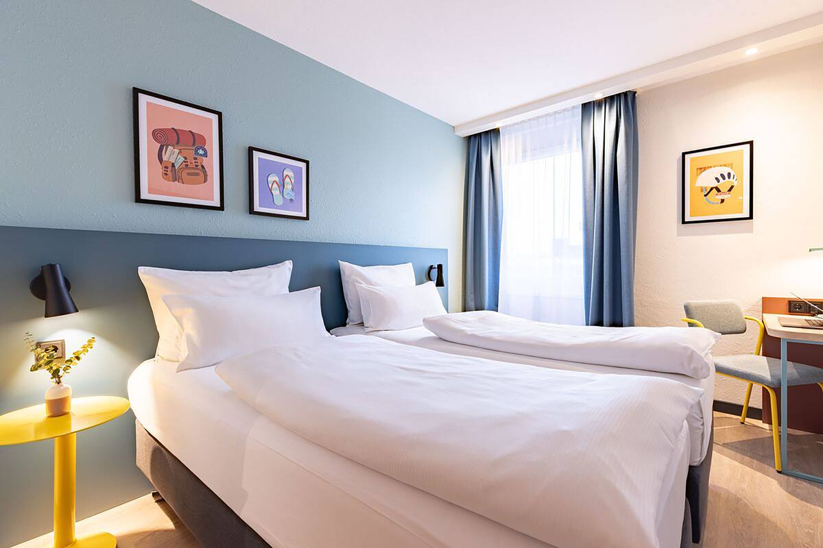Habitación de hotel con dos camas, un escritorio, una silla y obras de arte en las paredes.