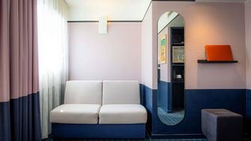 Ein Zimmer mit einer Couch, einem kleinen Hocker, einem Spiegel und einem Regal mit einem Buch.