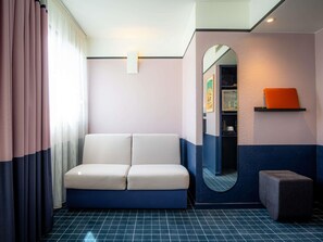 Une pièce comprenant un canapé, un petit pouf, un miroir et une étagère avec un livre.