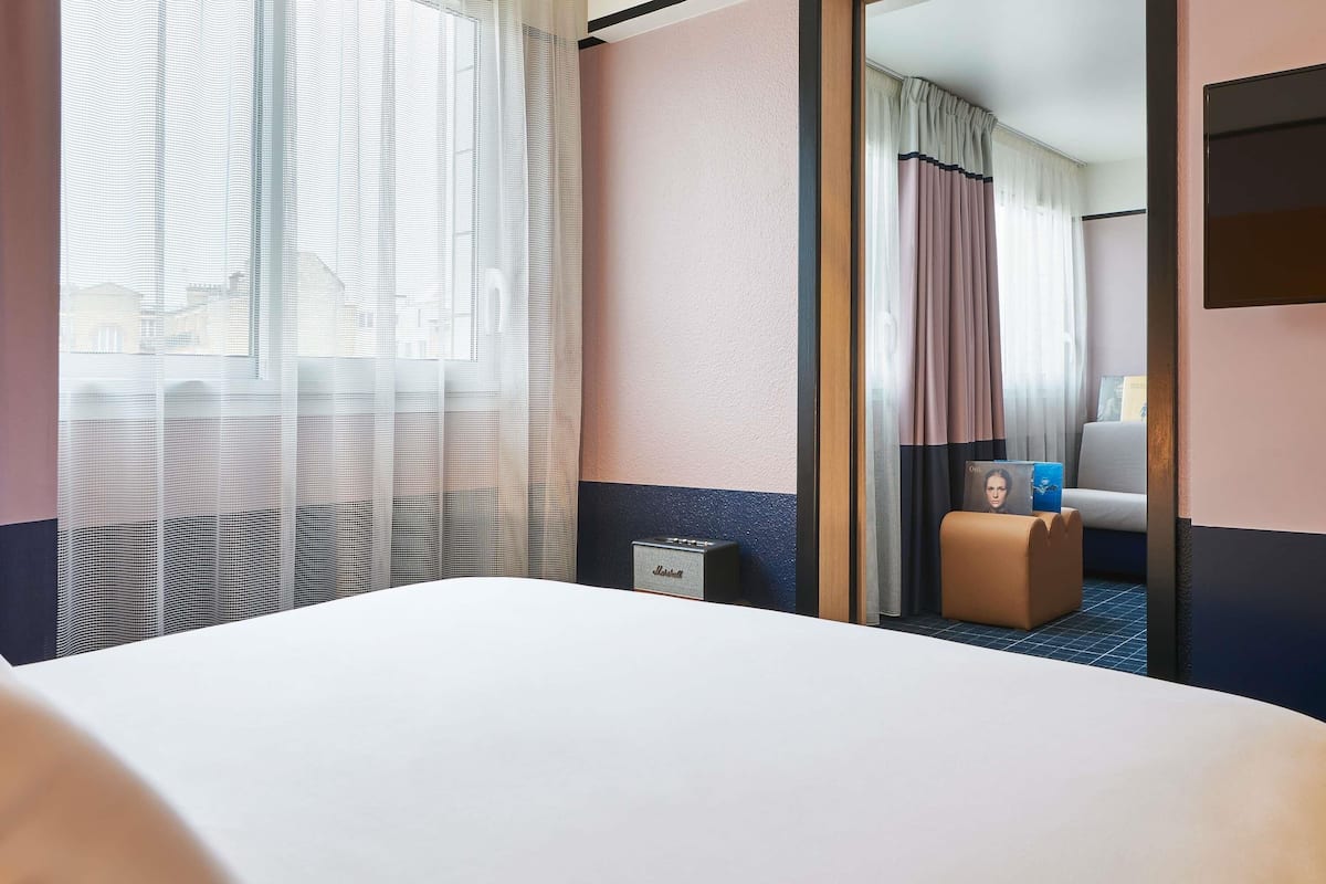 A hotel room with a bed, a desk, a chair, and a mirror.